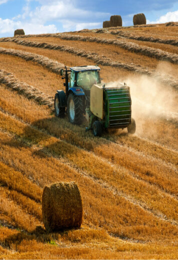 a hay baler in a field making bales of hay against a clear blue Alberta sky