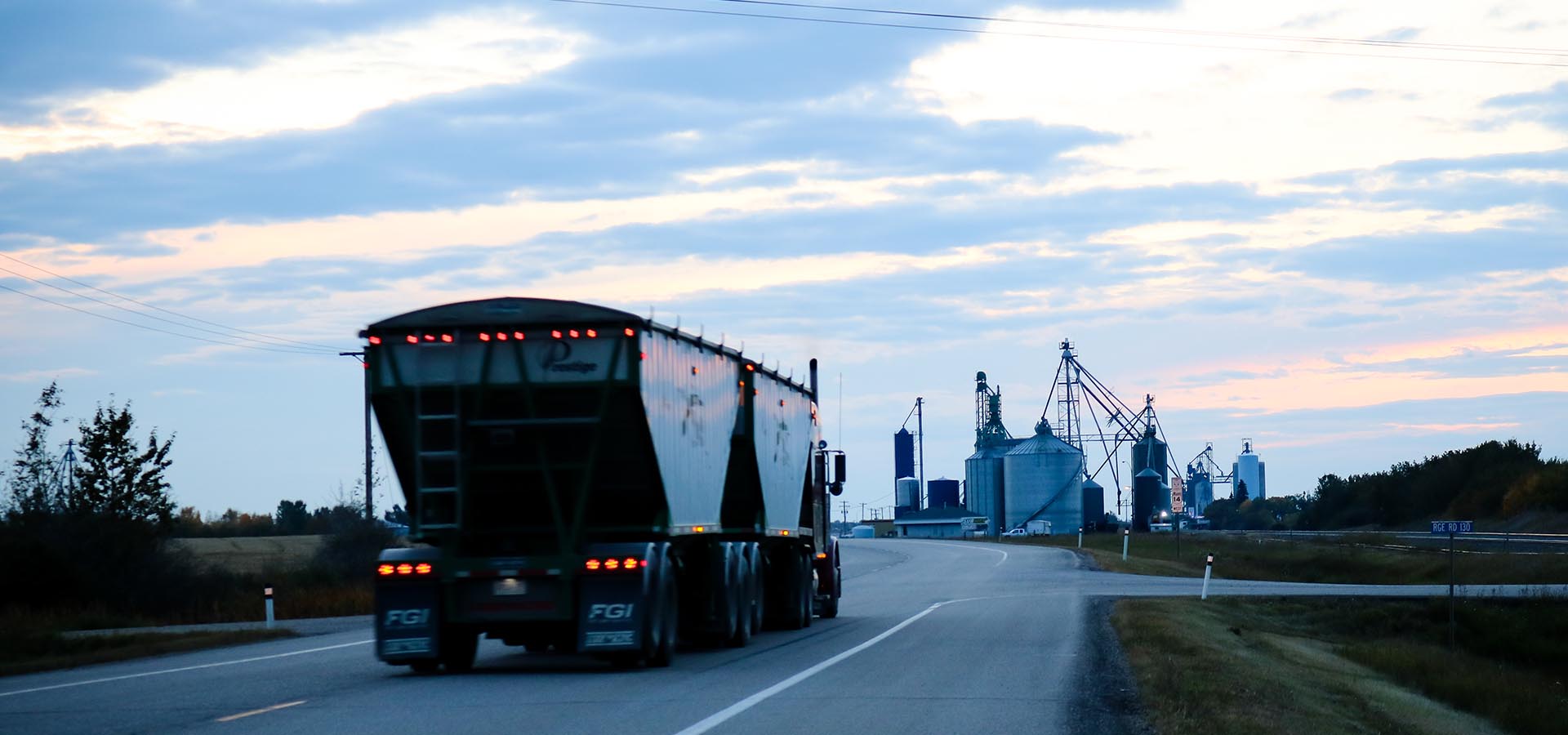 semi on a highway at dusk driving toward city buildings in the background